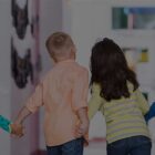 Four children hold hands in a school hallway with their backs to the camera