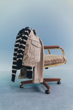 A striped long sleeve sweater and light grey Levi's® denim jacket hang on the back of a rolling office chair in front of a pale blue background.