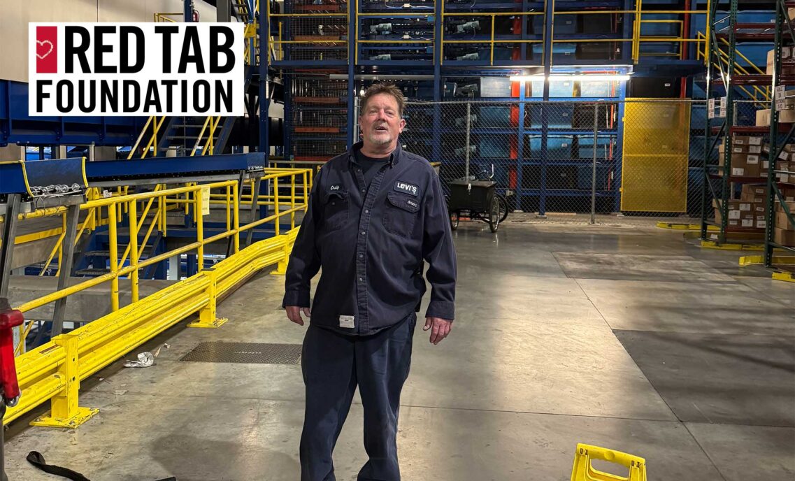 LS&Co. warehouse technician stands inside a warehouse. A Red Tab Foundation logo sits in the top left corner.