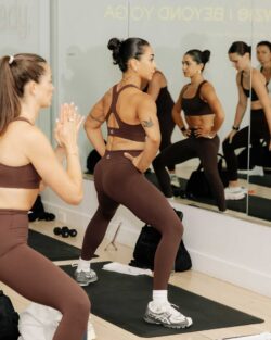 A photo of people wearing brown activewear sets by Beyond Yoga®, taking an exercise class on mats in a mirrored studio