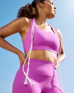 A photo of a person wearing a matching pink activewear set from the Beyond Yoga® glozone collection with wired headphones draped around their neck