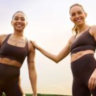 A photo of two people smiling at the camera wearing matching Beyond Yoga® glozone activewear sets in brown