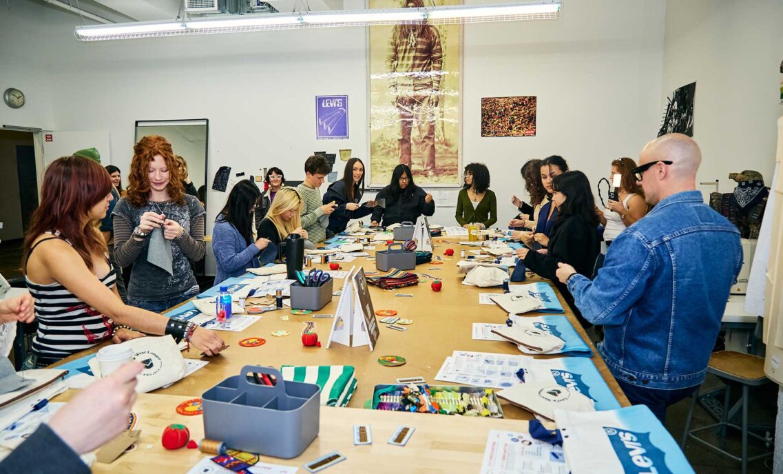 A group of San Francisco high school students gather around a large table with sewing supplies and print out sewing tutorials at a Levi's Wear Longer Project workshop