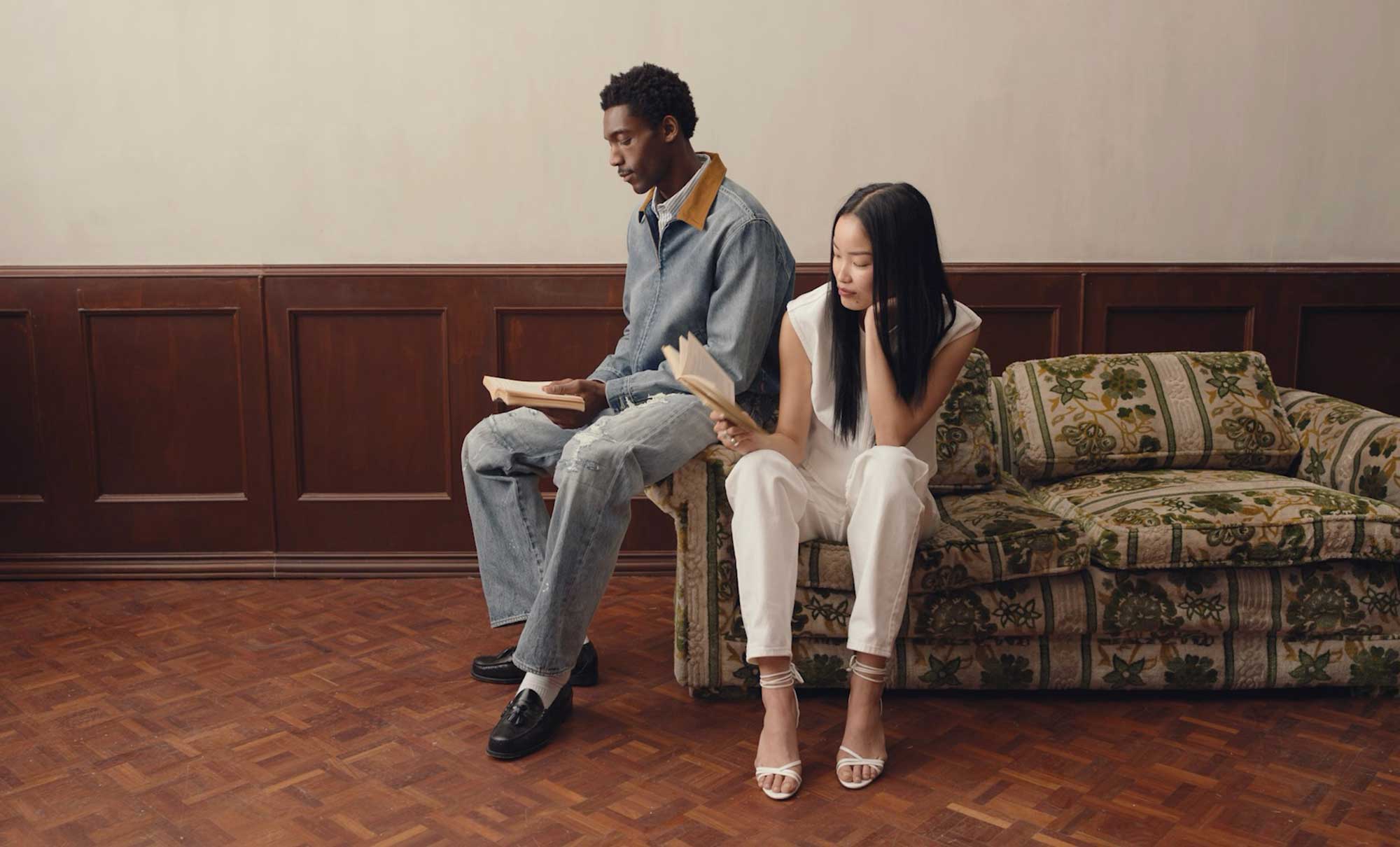 Two people pose on a couch reading books wearing Levi's® outfits