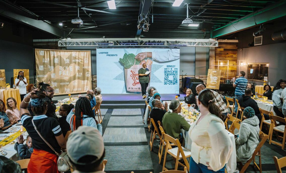 Pastor Mike, executive director of LIVE FREE USA, stands on stage in front of people sitting at tables as part of LIVE FREE’s Sunday Dinner series